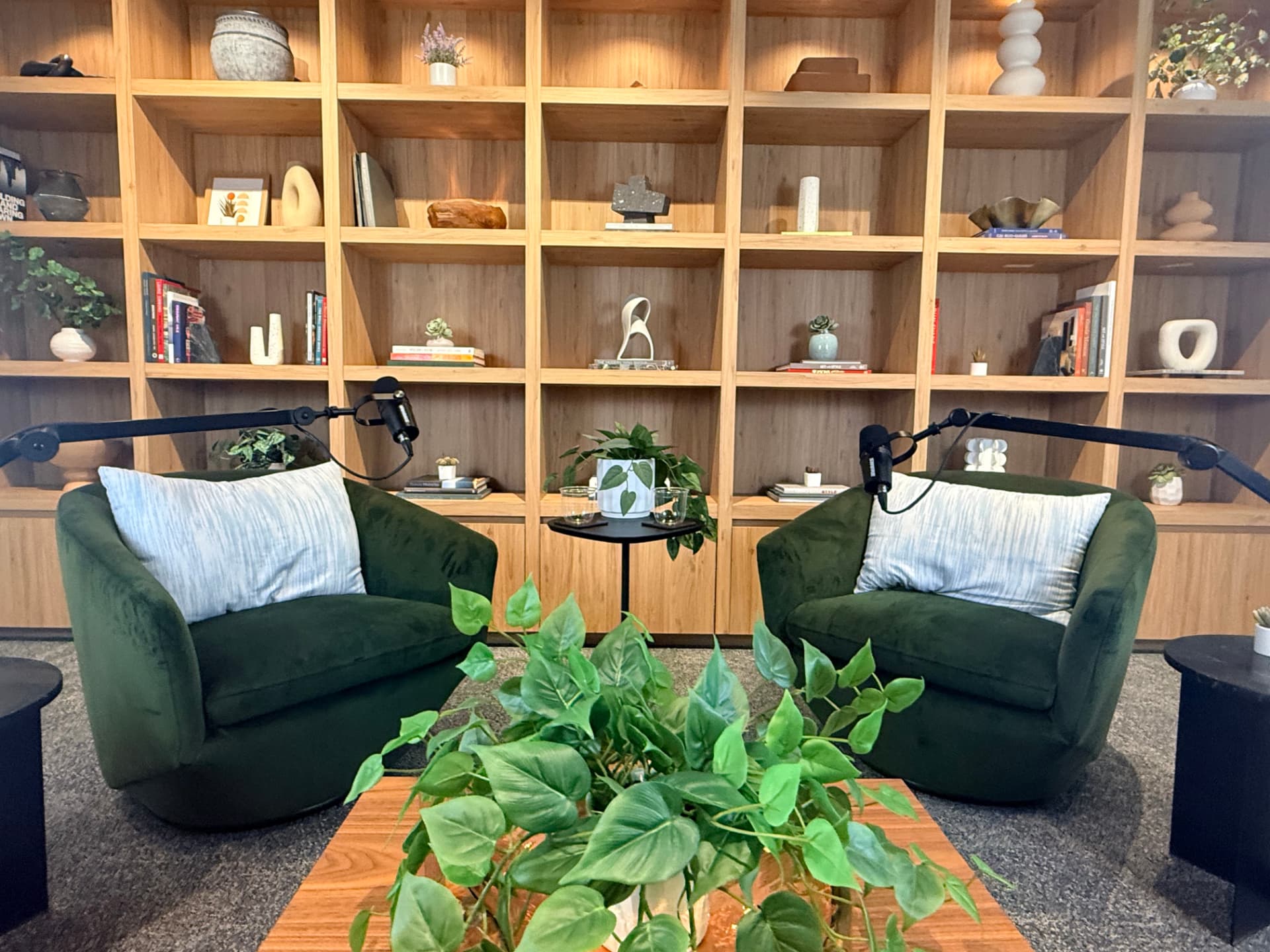 Podcast studio at 1400 K Street with green velvet chairs, boom microphones, and a wood shelving backdrop