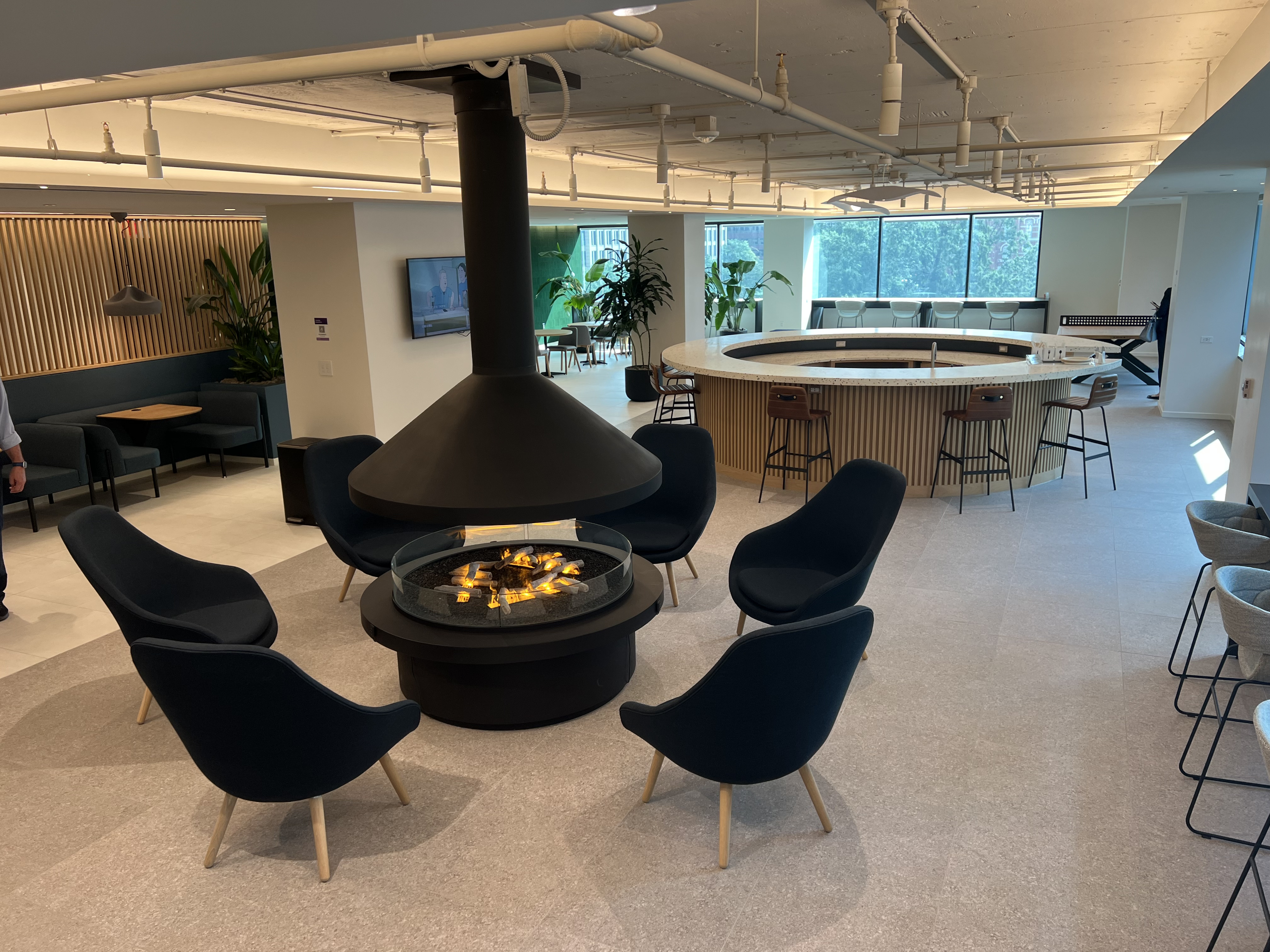 Modern lounge and event space with a central circular fireplace, curved bar, and floor-to-ceiling windows